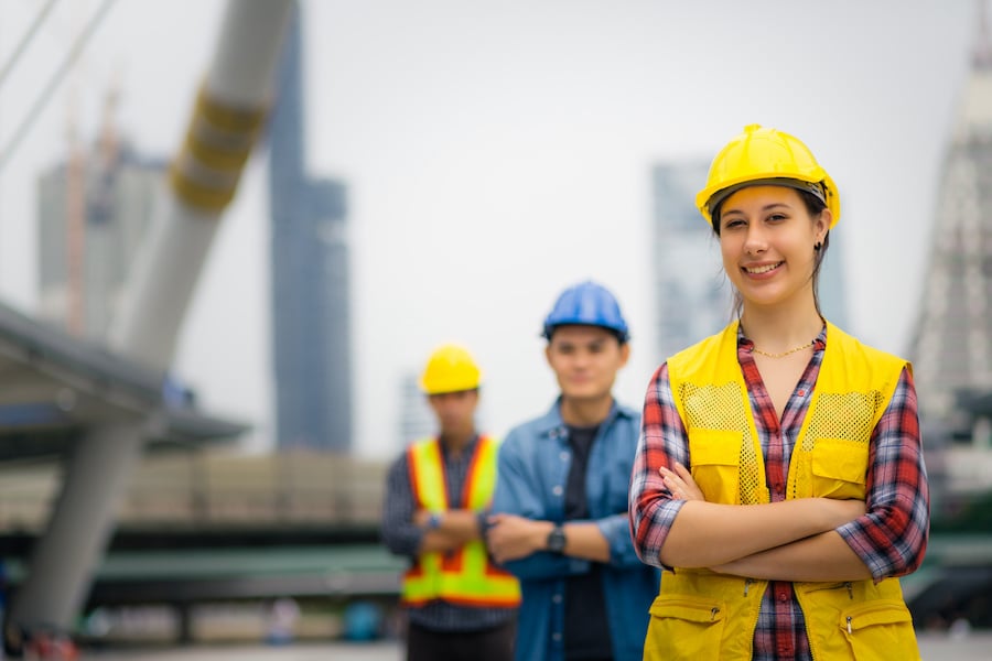 Three construction workers in safety vests and hard hats standing at a construction site