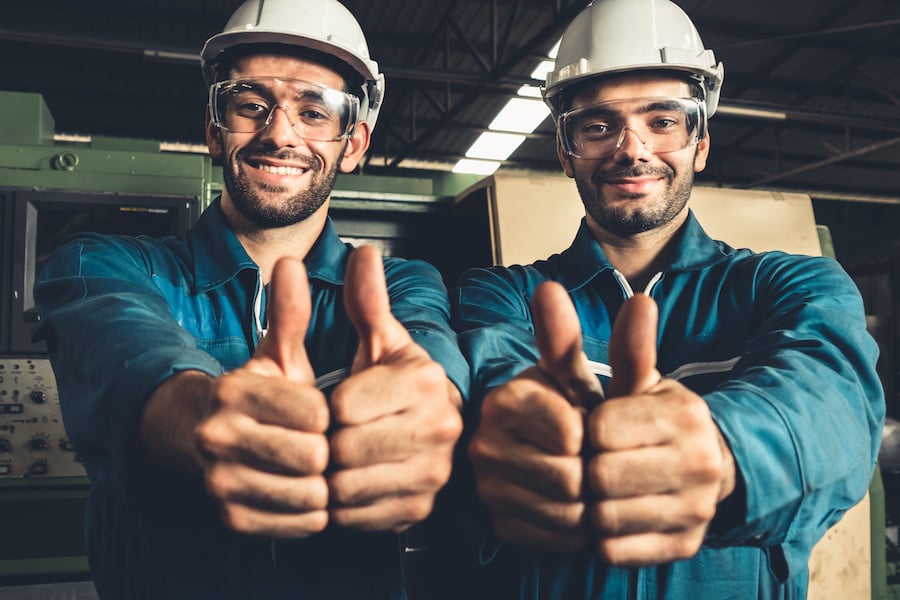 Two manufacturing workers with hard hats giving a thumbs up